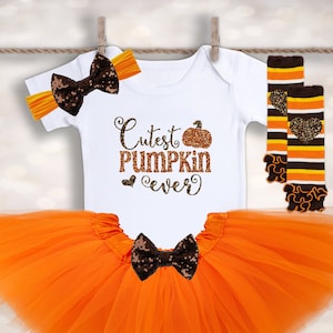 May include: Orange tulle tutu skirt, white bodysuit with "Cutest Pumpkin Ever" text and a pumpkin graphic, orange and brown striped leg warmers with a brown bow, and a brown bow headband with orange trim.