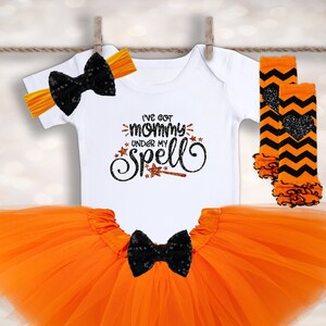 May include: Orange and black Halloween baby outfit with a tutu, leg warmers, headband, and a white onesie that says "I've got mommy under my spell".