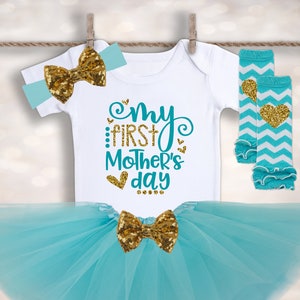 Puede incluir: Un conjunto para beb&eacute; ni&ntilde;a, que incluye un body blanco con el texto "My First Mother's Day", una falda tut&uacute; turquesa, una diadema y calentadores de piernas. El conjunto presenta lazos de lentejuelas doradas y detalles de coraz&oacute;n. Los calentadores tienen un patr&oacute;n de chevron.