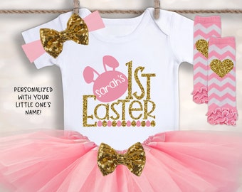 May include: Pink and gold Easter baby girl outfit with a tutu, headband, leg warmers, and a onesie that says "Sarah's 1st Easter".
