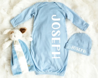 May include: A light blue baby gown with long sleeves and the name "JOSEPH" printed vertically down the back. A matching light blue hat with the same name printed on the front. A light blue and white plush toy is also included.