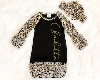 May include: Black baby gown with leopard print sleeves and a gold glitter name "Charlotte" on the front. The gown has a ruffled hem and comes with a matching leopard print headband.