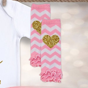 May include: Pink and white chevron leg warmers with gold glitter hearts. The leg warmers have a ruffled trim.