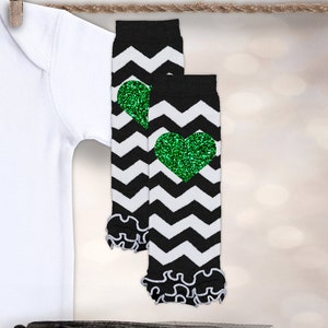 Op de afbeelding: Een paar zwart-witte chevron beenwarmers met groene glitterhartjes. De beenwarmers hebben een gerimpelde rand.