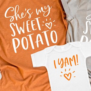 Puede incluir: Dos camisetas con tem&aacute;tica de Acci&oacute;n de Gracias. La camiseta m&aacute;s grande es naranja y dice "She's my sweet potato" con un peque&ntilde;o coraz&oacute;n. La camiseta m&aacute;s peque&ntilde;a es blanca y dice "I yam!" con un coraz&oacute;n.