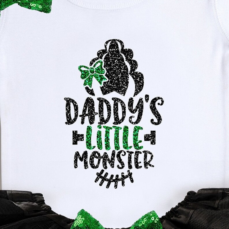 Op de afbeelding: Witte romper met een zwart en groen glitterontwerp met de tekst "Daddy's Little Monster" met een groene strik en een zwart en groen glittermonsterhoofd.