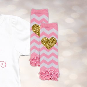 May include: A pair of pink and white chevron leg warmers with gold glitter hearts. The leg warmers have a ruffled edge.