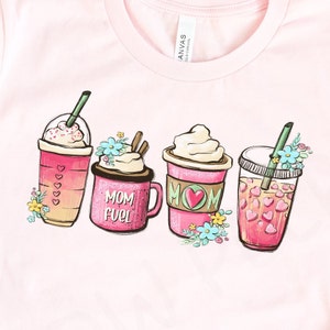 Op de afbeelding: Roze T-shirt met een afbeelding van vier verschillende koffiedrankjes. De drankjes zijn versierd met hartjes, bloemen en de tekst "Mom Fuel".