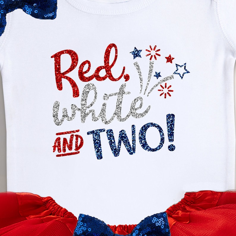 May include: Red, white and two! A white onesie with red, white, and blue glitter text and a firework design. The onesie is paired with a red tulle skirt and a blue sequin bow.