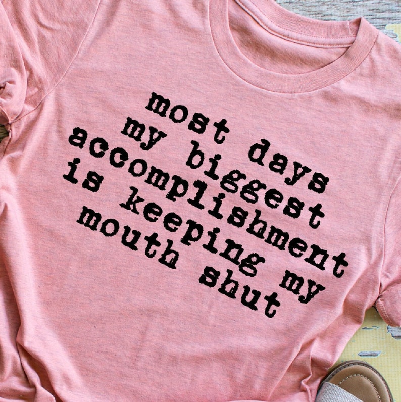 May include: Pink t-shirt with black text that reads "Most days my biggest accomplishment is keeping my mouth shut."