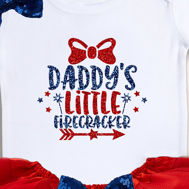 May include: White baby onesie with red and blue glitter text that says "Daddy's Little Firecracker" with a red glitter bow and a red and blue glitter arrow. The onesie is paired with a red tulle skirt and a blue sequin bow.