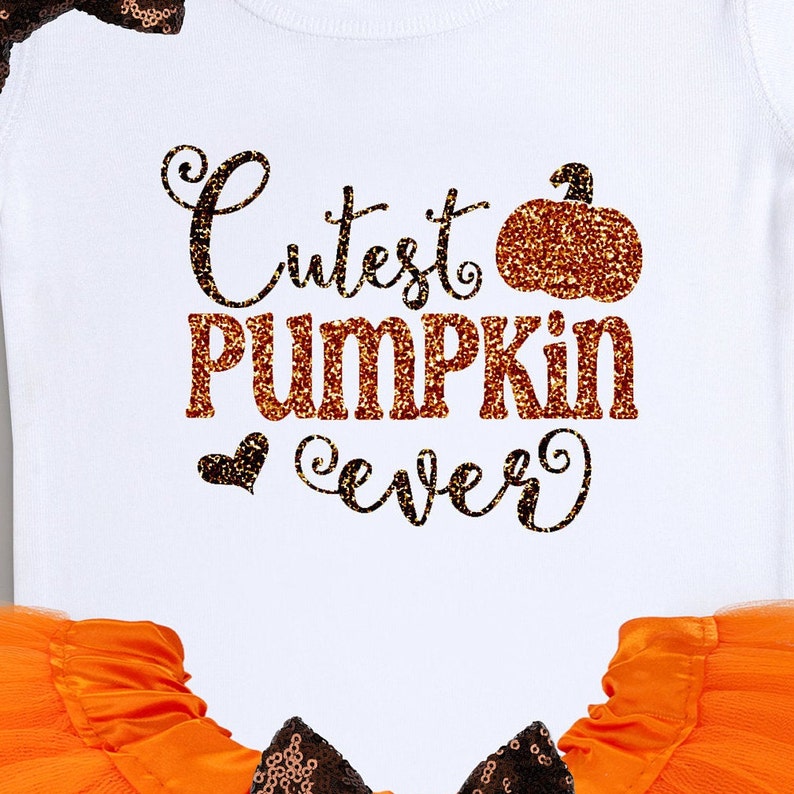 May include: A white onesie with the text "Cutest Pumpkin Ever" in brown and orange glitter. The onesie is paired with an orange tulle skirt and a brown bow.
