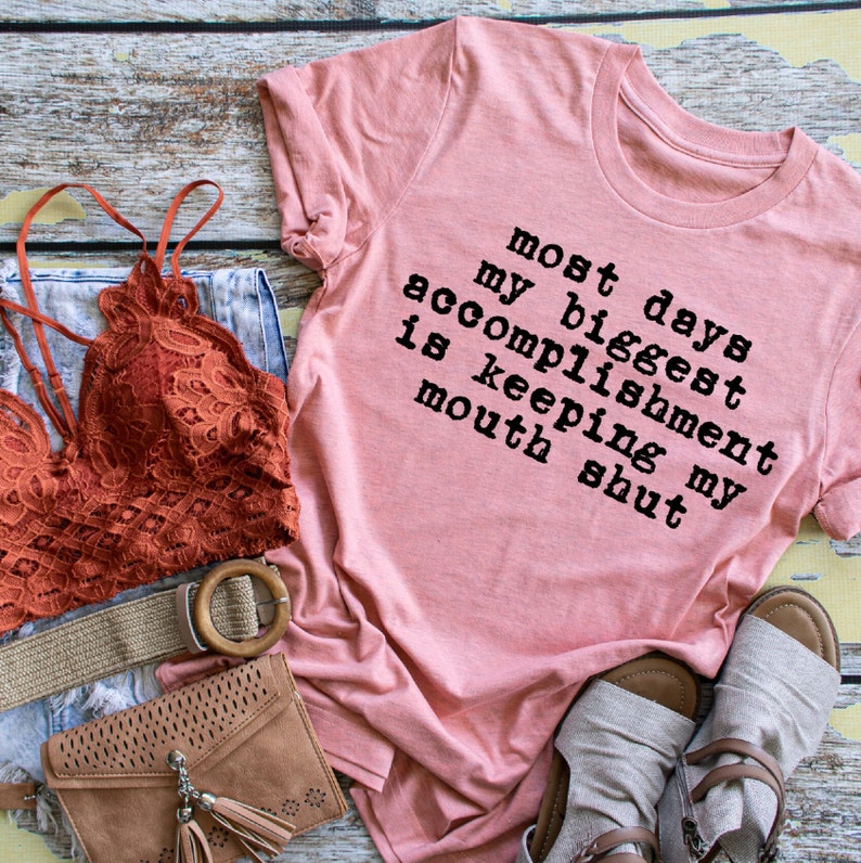 May include: A pink t-shirt with the text "most days my biggest accomplishment is keeping my mouth shut" printed on it.