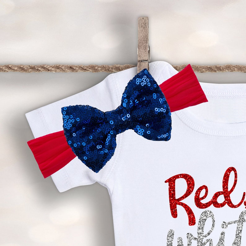 May include: White t-shirt with red glitter text that says "Red, White & Blue" and a blue sequin bow with a red headband.