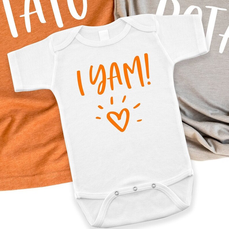 Puede incluir: Un body blanco para beb&eacute; con el texto "I YAM!" en naranja con un peque&ntilde;o coraz&oacute;n naranja y un dise&ntilde;o de brillo.