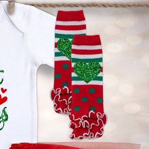 May include: Red and green striped leg warmers with green glitter hearts. The leg warmers have a red and white ruffle at the bottom.