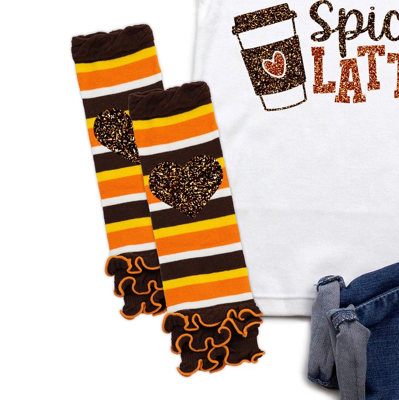 May include: Two striped leg warmers with brown, orange, and white stripes, each featuring a glitter heart. The leg warmers have ruffled edges. A white shirt with a glitter coffee cup graphic and the words "Spiced LATTE" is visible.