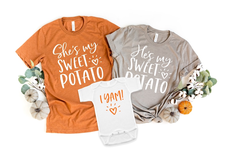 Puede incluir: Tres camisetas con tem&aacute;tica de Acci&oacute;n de Gracias. Las camisetas para adultos son naranja y gris con el texto "She's my sweet potato" y "He's my sweet potato". La camiseta para beb&eacute; es blanca con el texto "I yam!" y un coraz&oacute;n.