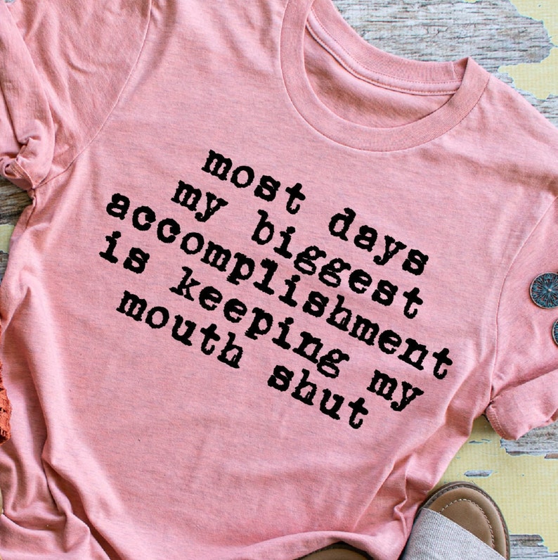 May include: A pink t-shirt with the text "Most days my biggest accomplishment is keeping my mouth shut" printed in black.