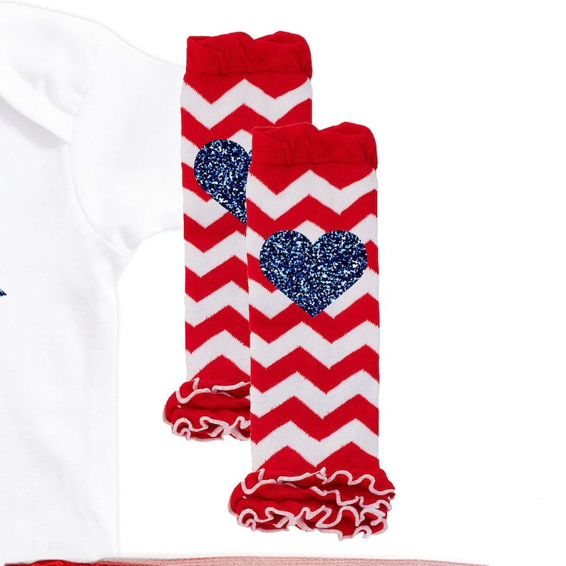 May include: Red and white chevron leg warmers with a blue glitter heart on each. The leg warmers have a ruffled edge.