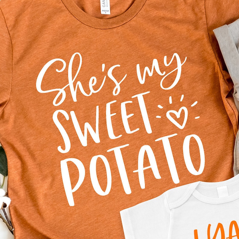 Puede incluir: Camiseta naranja con texto blanco que dice "She's my sweet potato" con un peque&ntilde;o gr&aacute;fico de coraz&oacute;n.