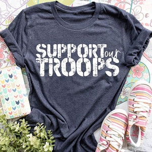 May include: A dark gray t-shirt with the text "SUPPORT our TROOPS" in white distressed lettering.