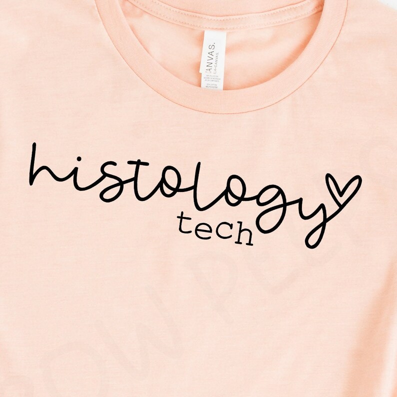 May include: A light pink t-shirt with the text "histology tech" in black cursive lettering with a small heart next to the word "technology".