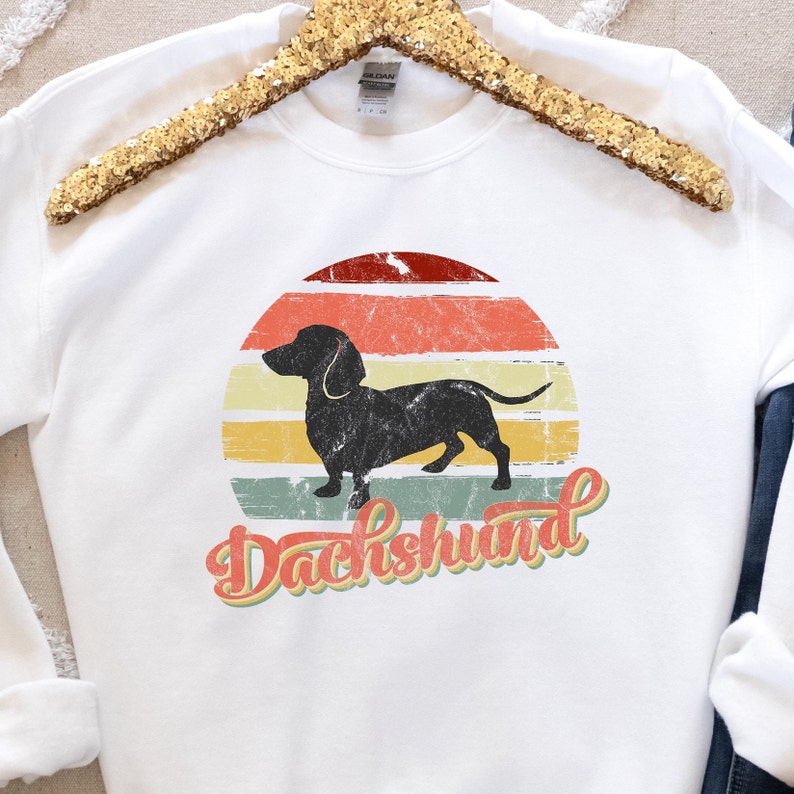 May include: White sweatshirt with a vintage-style graphic of a black dachshund silhouette in front of a sunset with the word "Dachshund" in a retro font.