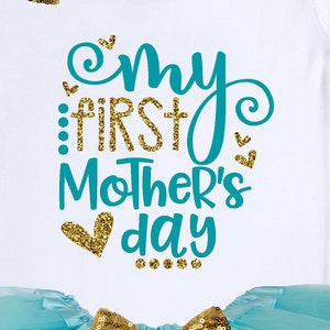 Puede incluir: Body de beb&eacute; blanco con el texto "My First Mother's Day" en verde azulado y purpurina dorada. El dise&ntilde;o incluye corazones y puntos. Un tut&uacute; azul claro con lentejuelas doradas es visible en la parte inferior.
