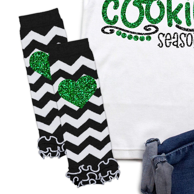 May include: Black and white chevron leg warmers with green glitter hearts. The leg warmers have a ruffled edge.