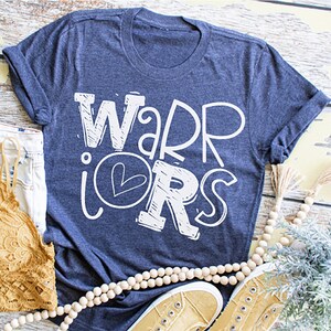 K&ouml;nnte beinhalten: Ein marineblaues T-Shirt mit dem Schriftzug "WARRIORS" in Wei&szlig;, wobei ein Herz in der Mitte des "O" platziert ist.