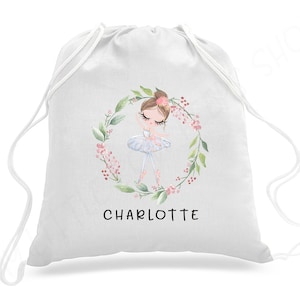 May include: White drawstring bag with a floral wreath design featuring a ballerina girl in a blue tutu. The bag has the name "CHARLOTTE" printed below the design.