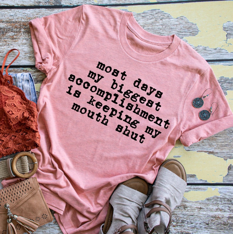 May include: Pink t-shirt with the text "Most days my biggest accomplishment is keeping my mouth shut" printed in black.