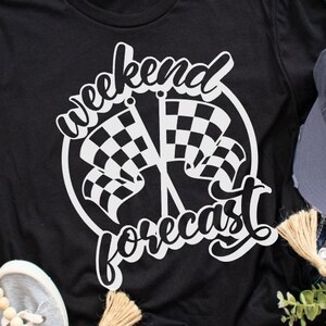 May include: Black t-shirt with a white graphic design of chequered flags and the text "Weekend Forecast".