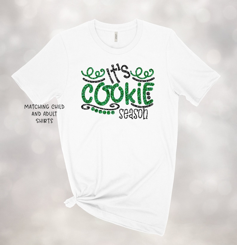 May include: White t-shirt with green glitter text that reads "It's Cookie Season".