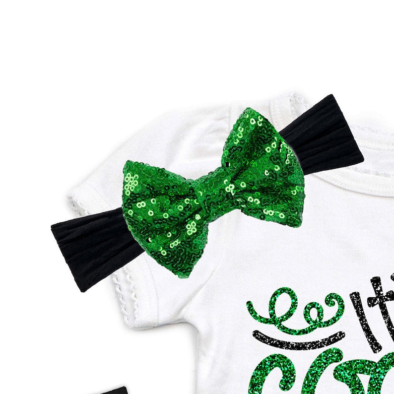 May include: A white shirt with a green sequin bow headband. The shirt has black sequin lettering that says "Let's Get Lit".