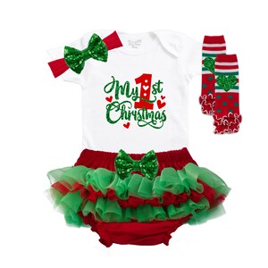 May include: A white onesie with red and green glitter text that says "My 1st Christmas". The onesie is paired with a red and green tutu, a green glitter bow, and red and green leg warmers.