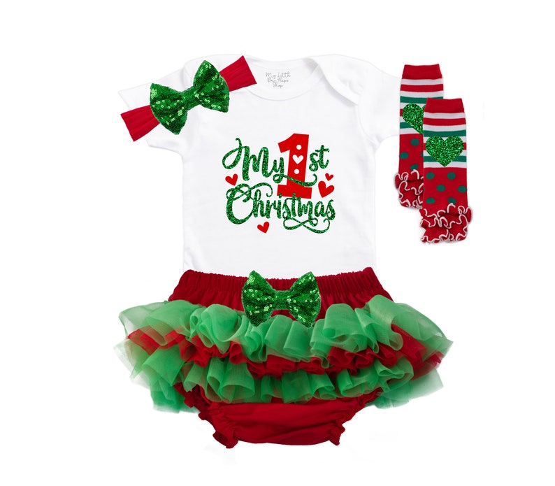 May include: A white onesie with red and green glitter text that says "My 1st Christmas". The onesie is paired with a red and green tutu, a green glitter bow, and red and green leg warmers.