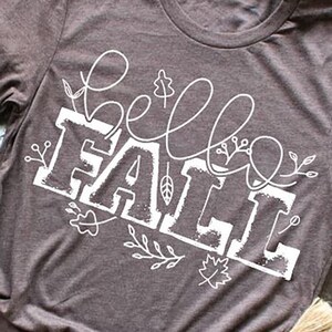 May include: A brown t-shirt with a white graphic that says "hello fall" with stylized leaves and vines.