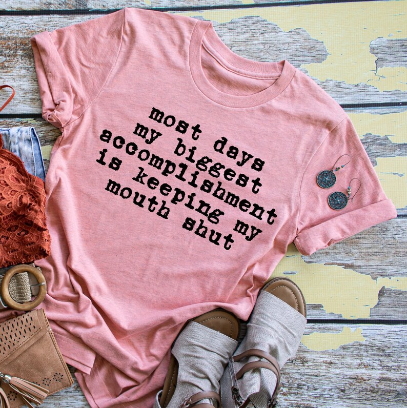 May include: A pink t-shirt with the text "most days my biggest accomplishment is keeping my mouth shut" printed in black.