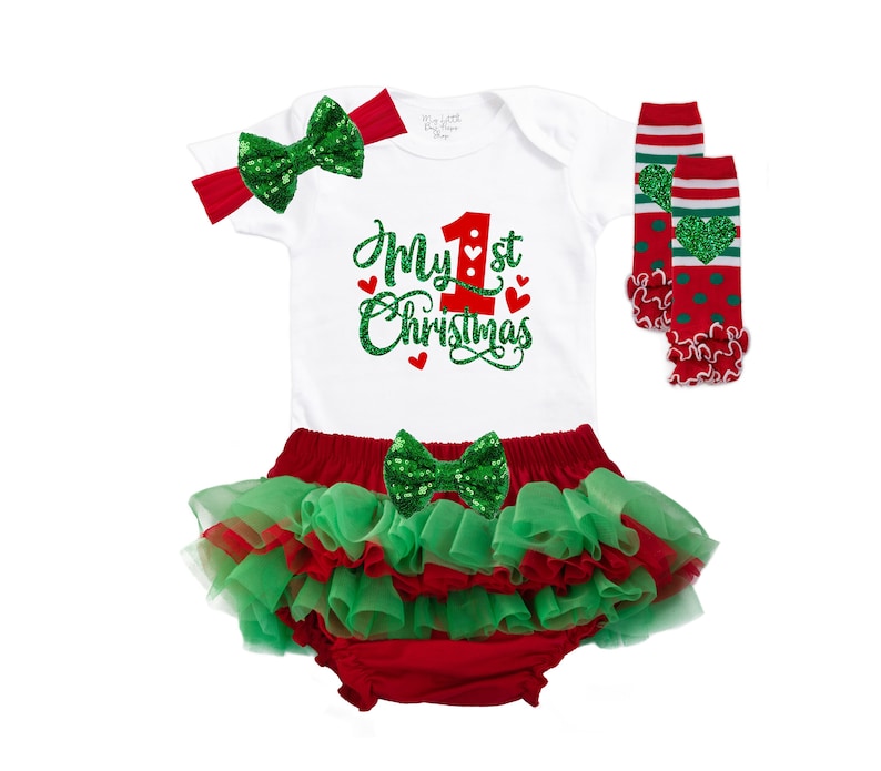 May include: A white onesie with red and green glitter text that says "My 1st Christmas". The onesie is paired with a red and green tutu, a green glitter bow, and red and green leg warmers.