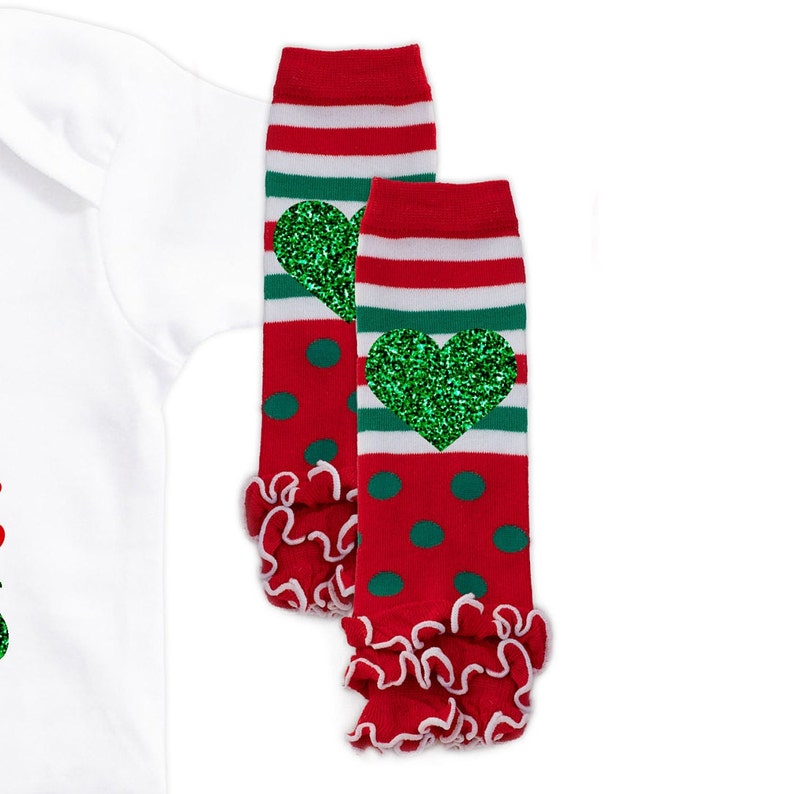 May include: Red and green striped leg warmers with a green glitter heart on each. The leg warmers have a white ruffle at the bottom.