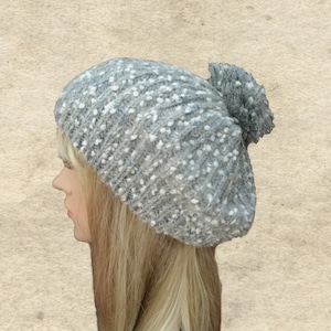 May include: A gray and white knitted beanie with a fluffy pom pom on top.
