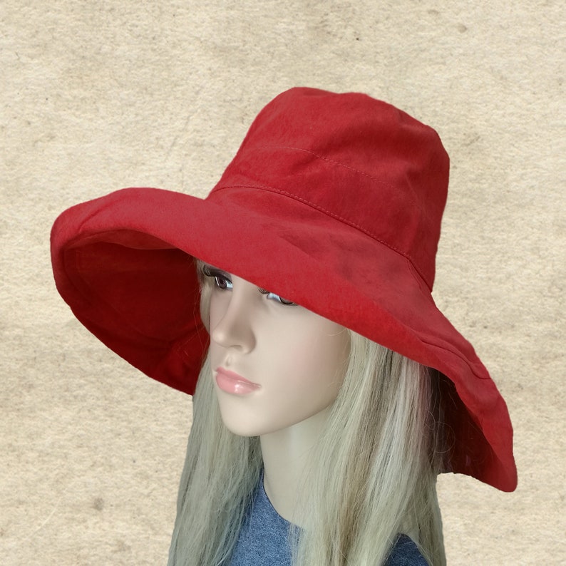 Puede incluir: Un sombrero de sol rojo de ala ancha con un dise&ntilde;o sencillo. El sombrero est&aacute; hecho de una tela suave y ligera y tiene un ala ancha que proporciona una amplia sombra.