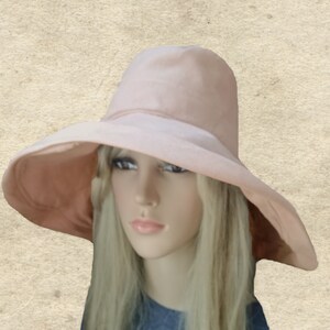 Puede incluir: Un sombrero de ala ancha de color rosa p&aacute;lido. El sombrero est&aacute; hecho de una tela suave y lisa y tiene un dise&ntilde;o sencillo.