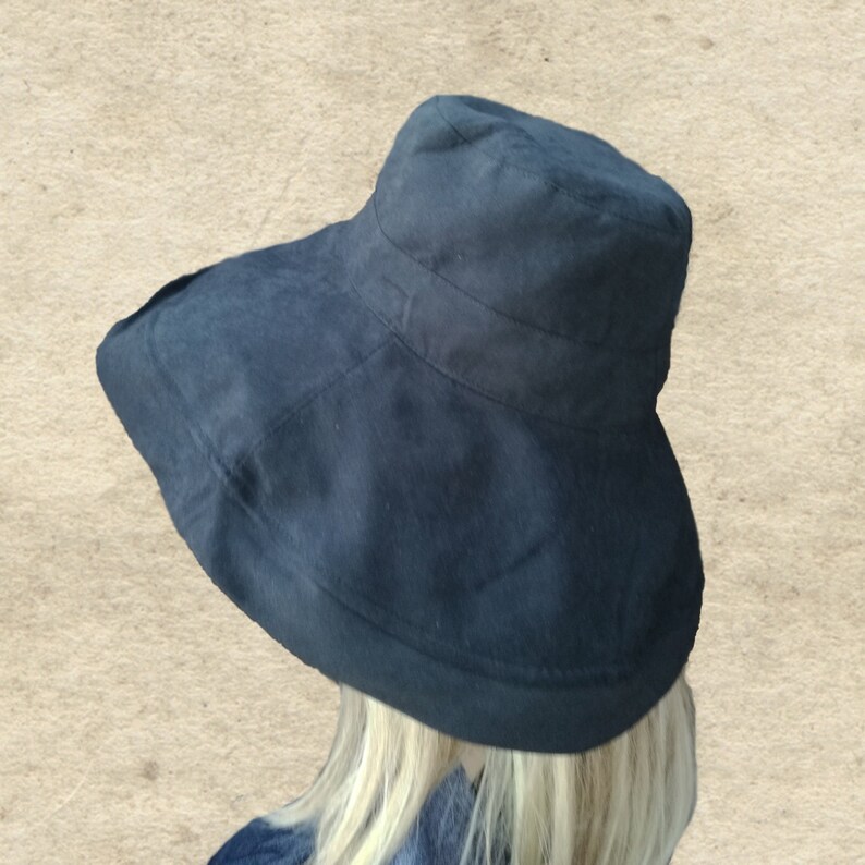Puede incluir: Un sombrero de sol negro de ala ancha con una corona ligeramente redondeada. El sombrero est&aacute; hecho de una tela suave y texturizada.