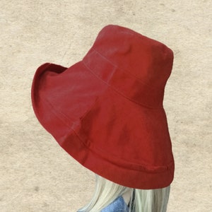 Puede incluir: Un sombrero de sol rojo de ala ancha con un dise&ntilde;o sencillo. El sombrero est&aacute; hecho de una tela suave y ligera y tiene un ala ancha que proporciona una amplia sombra.