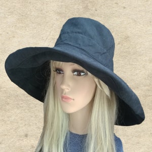 Puede incluir: Un sombrero de sol negro de ala ancha con una corona ligeramente redondeada. El sombrero est&aacute; hecho de una tela suave y texturizada.