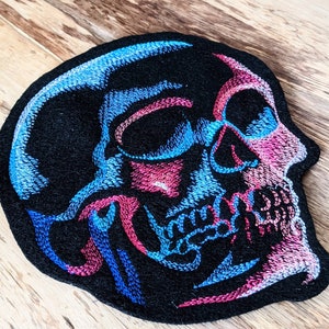 May include: Embroidered patch of a blue and pink skull with a black background.