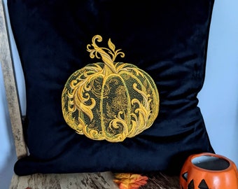 May include: A black velvet pillow with an embroidered gold pumpkin design. The pumpkin has intricate details and a leafy stem.